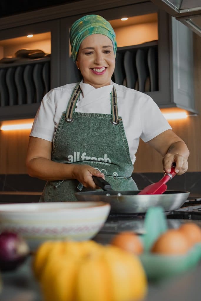 Chef Andréa Lícia sorrindo ao fogão da cozinha escola